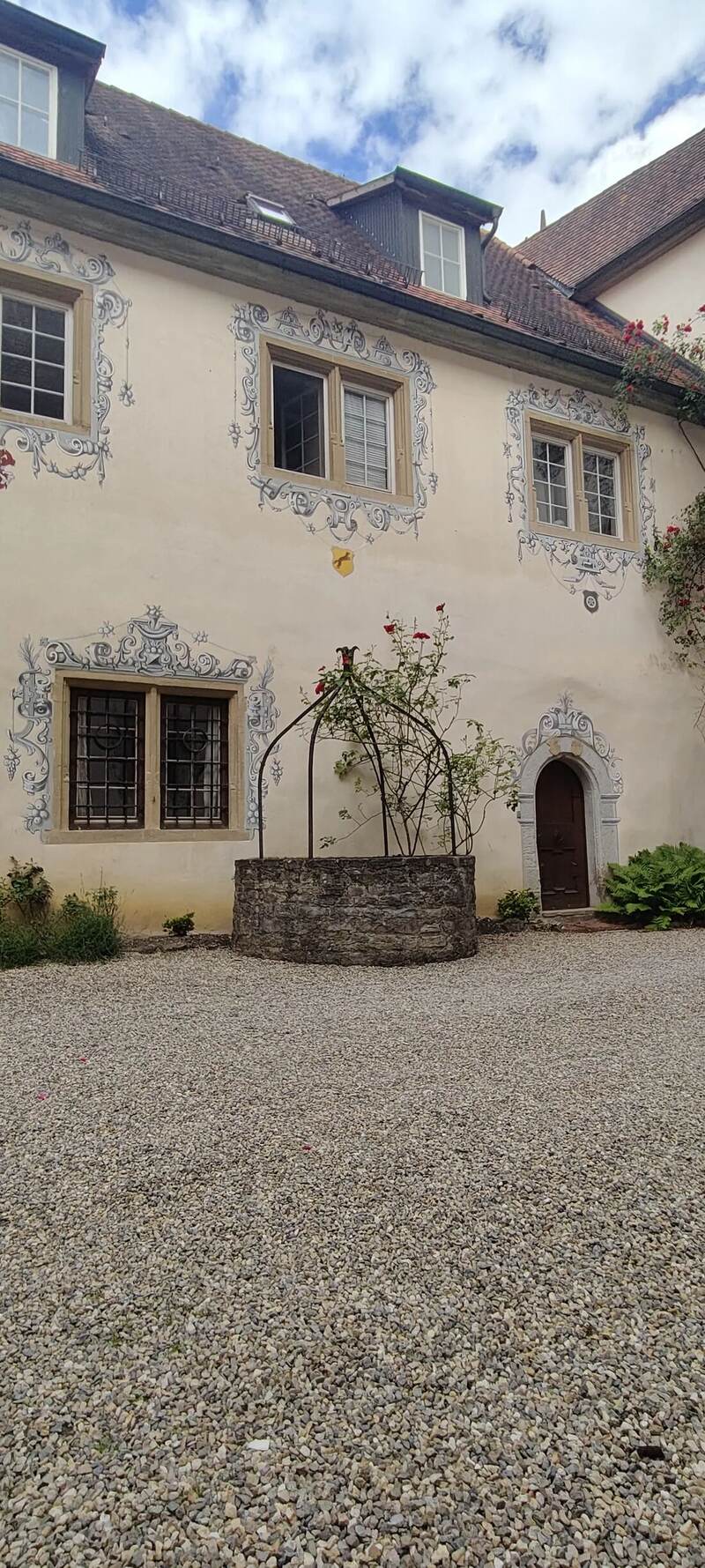 Bemalte Fassade von Schloss Laibach mit Ziehbrunnen und Rosenbogen, Innenhof