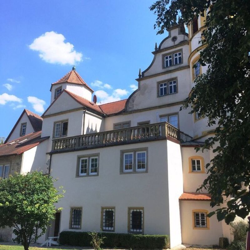 Hauptgebäude von Schloss Laibach mit Treppenturm, Balkon und rotem Ziegeldach vor blauem Himmel