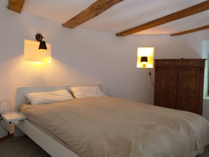 Doppelbett unter freiliegendem Holzbalken-Dachgebälk mit Nachttischlampen und altem Schrank